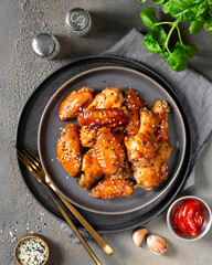 Homemade baked or fried chicken wings in barbecue sauce in a plate on the cooking table top view
