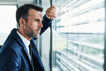 Thoughtful businessman looking through office window - Powered by Adobe