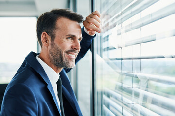 Successful businessman looking outside office window - obrazy, fototapety, plakaty