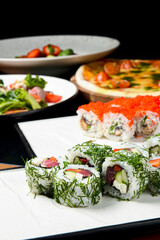 Sushi rolls with tuna, cucumber and cream-cheese in chopped dill. Served on a white plate over white background.