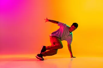 Gordijnen Portrait of young stylish man, break dancing dancer training in casual clothes isolated over gradient pink yellow background at dance hall in neon light. © master1305