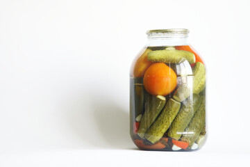 Preserved tomatoes and cucumbers in a large transparent three-liter jar on a white background. The concept of homework and farm harvest