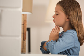 Fototapeta na wymiar Cute little girl with hands clasped together praying at home. Space for text