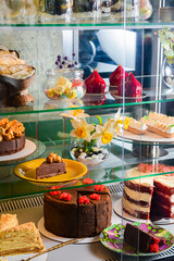 Various cakes with icing and desserts in refrigerated bakery case cabinet. Coconut shell dessert, chocolate cake.