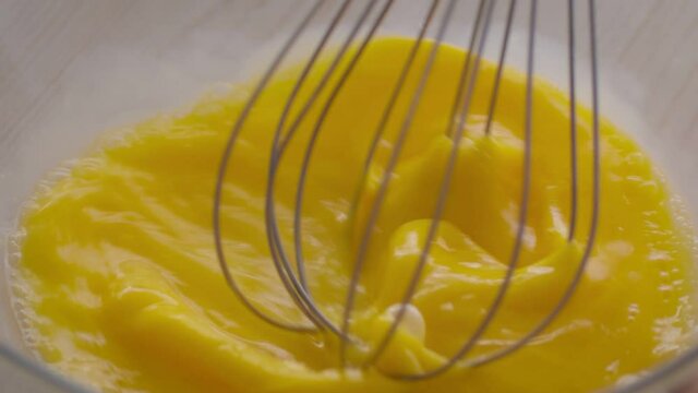 Cooking scrambled eggs. Close up shot of chef mixing egg yolks with metal whisk in bowl, preparing dough at kitchen