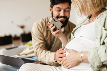 White man touching his pregnant wife's belly while sitting on couch