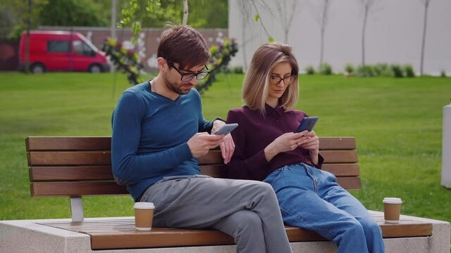 Couple friends using smartphones outdoor park, man and woman holding phones in hands texting shopping in app checking social media, mobile technology lifestyle and addiction concept. Coffee Break.