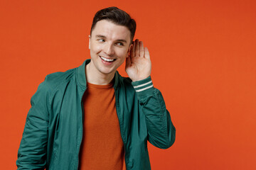 Curious nosy fun young brunet man 20s wears red t-shirt green jacket try to hear you overhear...