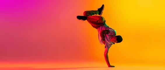 Tuinposter Flyer with young stylish man, break dancing dancer training in casual clothes isolated over gradient pink yellow background at dance hall in neon light. © master1305