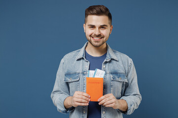 Traveler tourist overjoyed excited jubilant smiling young brunet man 20s wears denim jacket hold passport boarding tickets isolated on dark blue background studio portrait. Air flight journey concept.