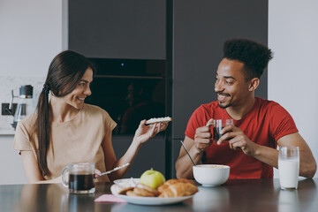 Fototapeta na wymiar Young couple two woman american african man 20s in casual clothes eat breakfast muesli drink coffee giving sandwich sit by table cooking food in kitchen at home together Healthy diet lifestyle concept