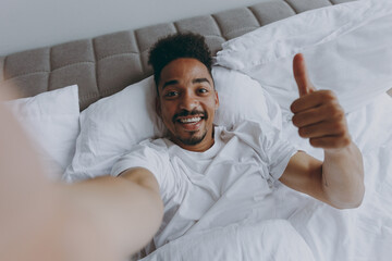 Close up young african american man in nightwear do selfie shot pov mobile phone show thumb up...