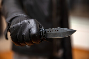Burglar holding a knife in gloved hand, armed robbery concept.