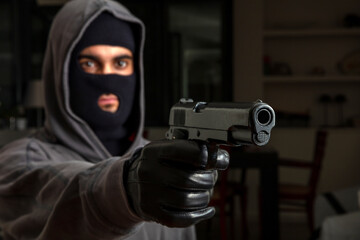 Hooded burglar holding a pistol, dark indoor background,