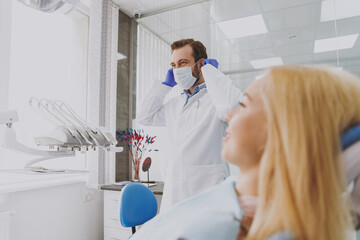 Naklejka premium Young male man doctor preparing before procedure for patient woman sitting at dentist office chair indoor light cabinet near stomatologist wait for oral examination Healthcare caries enamel treatment.