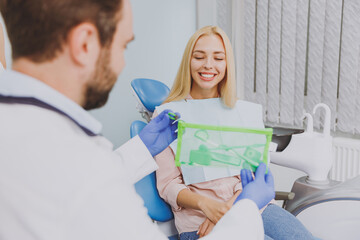 Obraz premium Close up stomatologist young man doctor wear gown give kit care braces grooming brushes for cleaning to patient caucasian woman sitting at dentist office chair indoor cabinet. Healthcare treatment