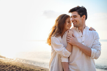 Smiling young couple two friends family man woman 20s in casual clothes hug girlfriend put head on boyfriend shoulder at sunrise over sea sand beach ocean outdoor seaside in summer day sunset evening. - obrazy, fototapety, plakaty