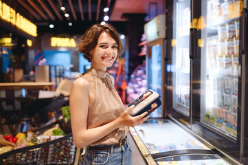 Young fun woman in casual clothes shopping at supermaket grocery store buy choose products stand near refrigerator hold container read ingredient shelf life inside hypermarket Purchasing food concept.