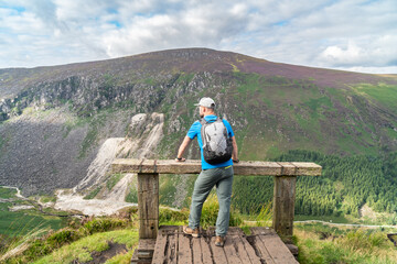 Fototapeta na wymiar Male resting on the hill at the Glendalough Valley. Panoramic idyllic view. County Wicklow Upper lake from miners way, Glenealo valley, Wicklow way, County Wicklow, Ireland.