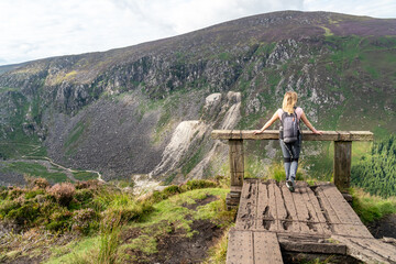 Fototapeta na wymiar Girl resting on the hill at the Glendalough Valley. Panoramic idyllic view. County Wicklow Upper lake from miners way, Glenealo valley, Wicklow way, County Wicklow, Ireland.