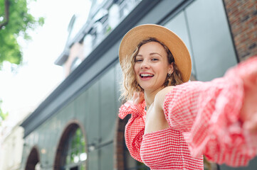 Close up young smiling happy beautiful woman 20s wearing pink dress hat doing selfie shot pov on mobile phone walk in city stand outdoor near brick building People urban summer time lifestyle concept.