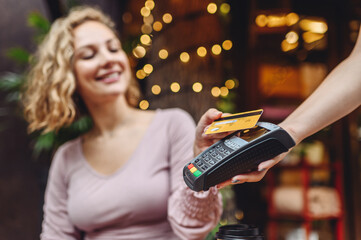 Young happy woman in casual clothes at cafe buy breakfast sit at table hold wireless modern bank payment terminal to process acquire credit card payments relax in restaurant during free time indoors - obrazy, fototapety, plakaty