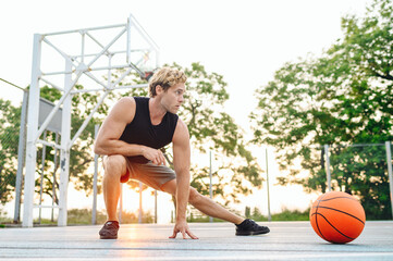 Full size young sporty sportsman man 20s in shorts sports clothes training do stretch exercise for legs sit at floor play with ball at basketball game playground court Outdoor courtyard sport concept