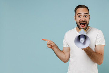 Young happy man in white t-shirt hold scream in megaphone announces discounts sale Hurry up point index finger aside on workspace area isolated on plain pastel light blue background studio portrait - obrazy, fototapety, plakaty