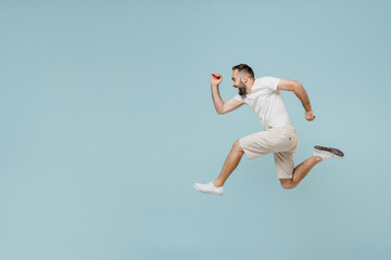 Fototapeta na wymiar Full length side view young excited happy sportsman caucasian man 20s wearing casual white t-shirt jump high run fast hurrying up isolated on plain pastel light blue color background studio portrait