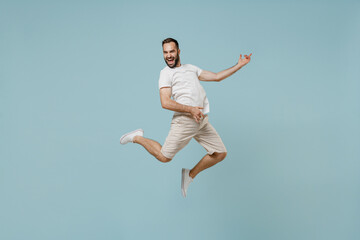 Fototapeta na wymiar Full length young overjoyed expressive rock singer happy caucasian man 20s wearing casual white t-shirt jump high playing guitar isolated on plain pastel light blue color background studio portrait