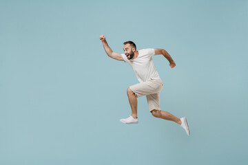 Fototapeta na wymiar Full length side view young excited happy sportsman runner man 20s wearing casual white t-shirt jump high run fast hurrying up isolated on plain pastel light blue color background studio portrait