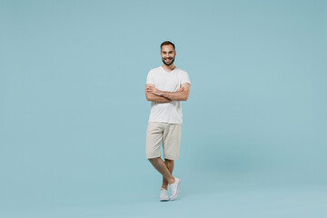 Fototapeta na wymiar Full length young smiling friendly cheerful happy man 20s wearing casual white t-shirt looking camera hold hands crossed folded isolated on plain pastel light blue color background studio portrait