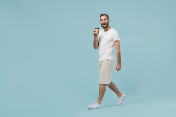 Fototapeta na wymiar Full length side view young happy man 20s wear casual white t-shirt hold takeaway delivery craft paper brown cup coffee to go walk isolated on plain pastel light blue color background studio portrait.