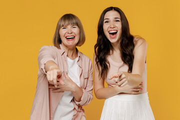 Two young daughter mother together couple women in casual beige clothes point index fingers camera on you laughing joking isolated on plain yellow background studio portrait. Family lifestyle concept.
