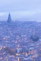 Fototapeta na wymiar Cityscape in old city changing light at dawn; Tower of the primate cathedral with the old town and its small streets of Toledo with fog and clouds, world heritage site, Spain. Vertical view