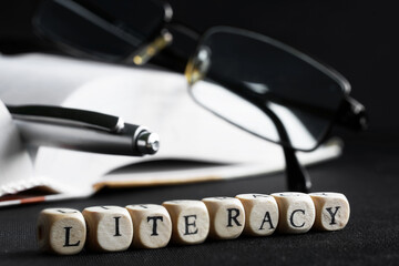 Literacy lettering next to glasses, an open thick book and a pen. The concept of literacy and learning in college or school. Macro. Shallow depth of field. Selective focusing