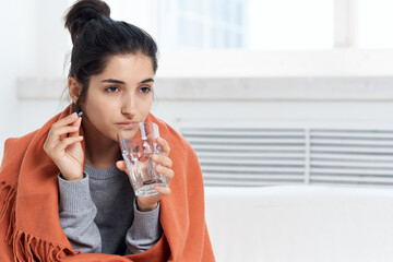 woman with a cold covered with a blanket sitting at home treatment