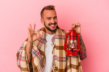 Young caucasian man with tattoos holding vintage lantern isolated on pink background  cheerful and...