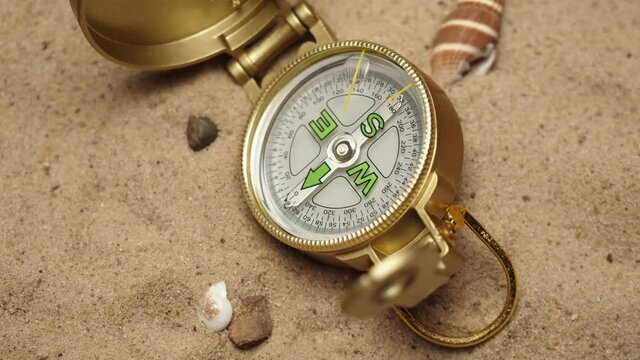 Gold compass on sand background close-up, focusing of golden compass. Traveling and tourism concept, navigation.
