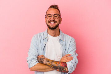 Young caucasian man with tattoos isolated on pink background  who feels confident, crossing arms with determination.