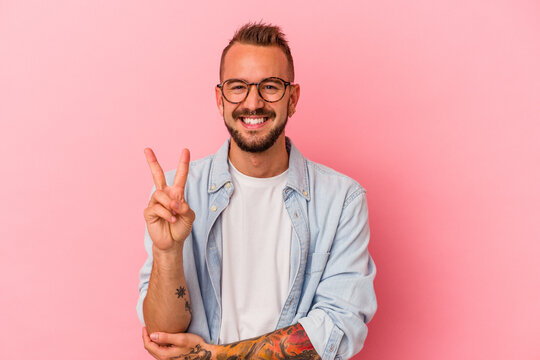 Young caucasian man with tattoos isolated on pink background  showing number two with fingers.