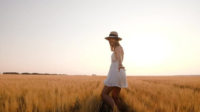 Happy free young woman runs in slow motion across field, touching ears of wheat with her hand. Wheat field on sunset background