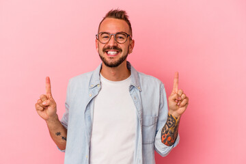 Young caucasian man with tattoos isolated on pink background  indicates with both fore fingers up...