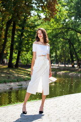 Young beautiful brunette girl in a white skirt posing in a summer park