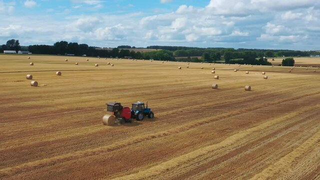 Blue tractor with red baler collects straw into bales.
Fly over a golden wheat field.  There are wonderful landscapes around the fields.