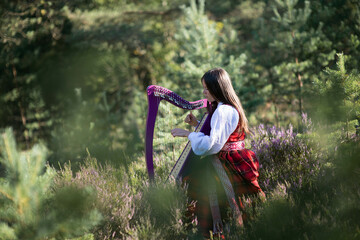 Beautiful young woman playing celtic harp and singing song in woodland
