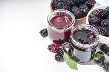 Sweet homemade blackberry jam in small glass jar on a white background, with fresh berries copy space