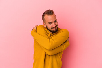 Young caucasian man with tattoos isolated on pink background  hugs, smiling carefree and happy.