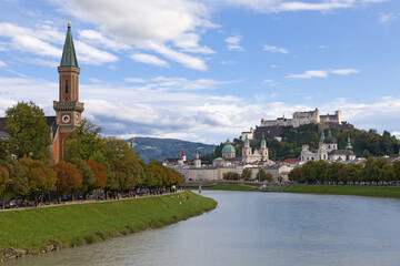 Fototapeta premium Panoramic urban scenery with famous Historic Centre and River Salzach embankment in Salzburg, Austria. Sunny autumn day, blue sky, clouds. Austrian ancient historical monuments. Touristic destination.
