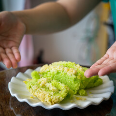 Obraz na płótnie Canvas Pandan green cake with butter crumbs in a white plate with hands holding. Top view.